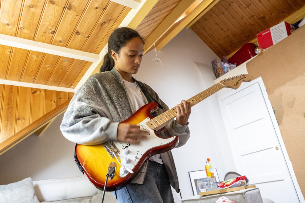 A focused young person playing an electric guitar in a cozy attic room.