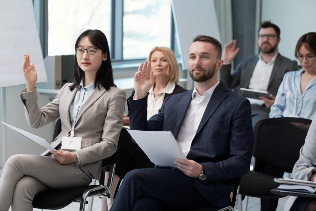 types of public speaking skills courses available that cater to different skill levels and needs Two young confident participants of conference raising hands to ask questions to speaker during presentation.