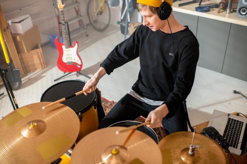 Handsome young musician in casualwear beating cymbals with wooden drumsticks for his online drum class