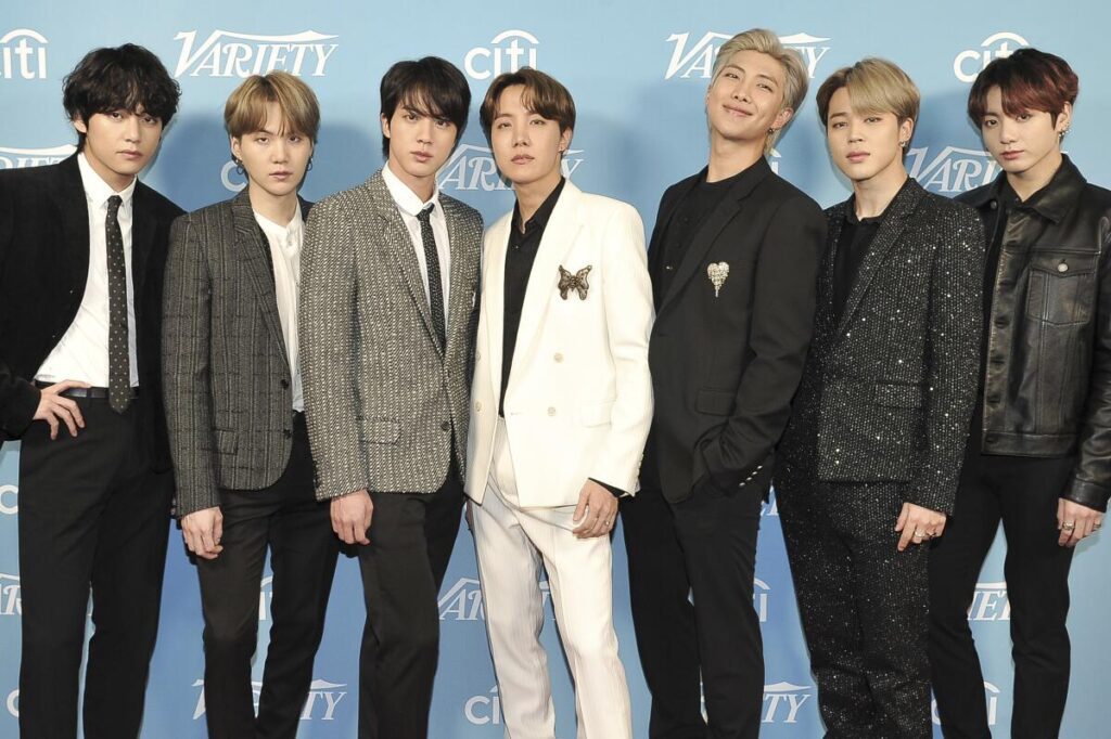 Members of a famous K-POP Band posing together on the red carpet in stylish suits, showcasing their global popularity and charismatic presence