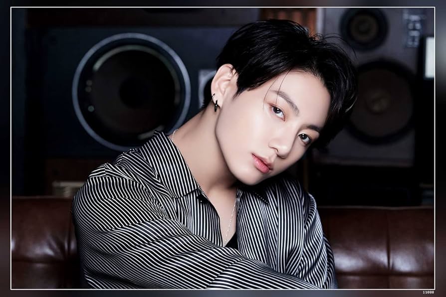 "A young man with black hair wearing a striped shirt poses indoors with a soft expression, highlighting his stylish look and musical charm.
