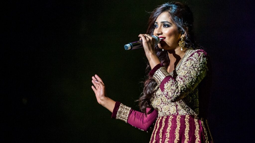 Shreya Ghoshal performing live on stage in a traditional maroon outfit, the iconic Indian playback singer with a soulful voice.