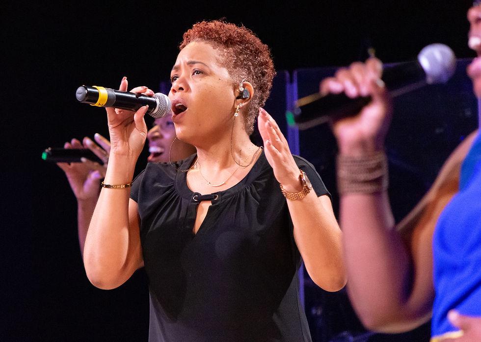 A worship singer standing on a church stage, holding a microphone, eyes closed in deep emotion, soft golden light shining from above, blurred congregation in the background, spiritual and peaceful atmosphere, warm tones, cinematic lighting, depth of field, highly detailed, realistic, 4k, inspirational mood, worship setting