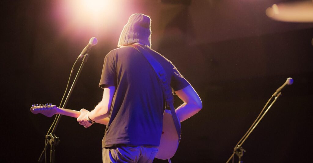 Musician playing guitar on stage during a live worship or concert performance with bright stage lights and microphones in the background.Building a Guitar Section for Your Church
