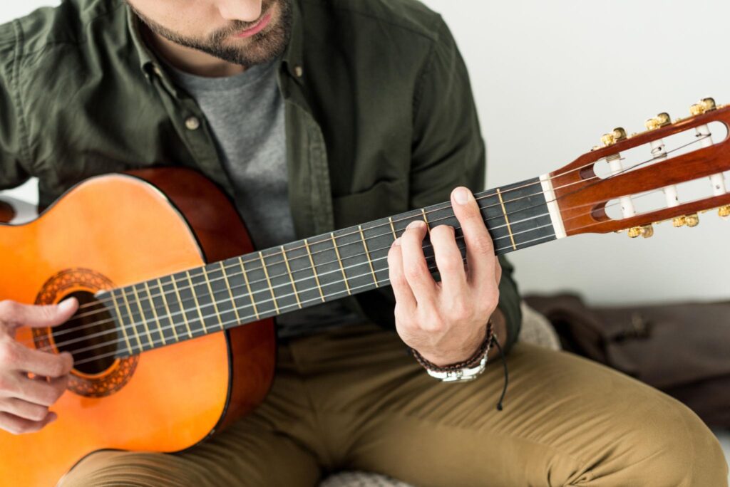 Beginner guitarist practicing a barre chord on an acoustic guitar while learning proper finger placement and technique for Understanding Barre Chords Without Frustration.