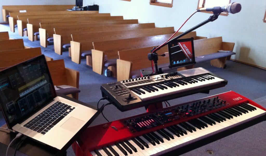 Worship keyboardist using layered keyboard patches and ambient textures during a church worship service with stage lighting and live musicians.