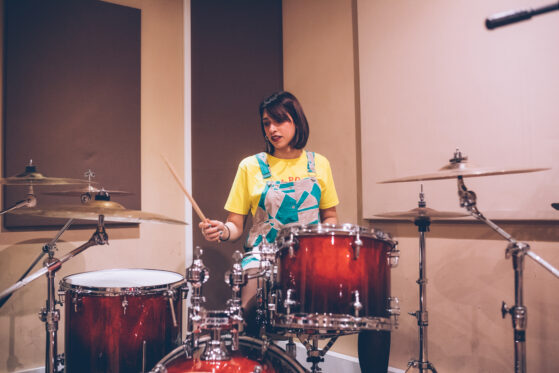 Young woman musician playing drum set holding drumstick - Music band performing in a recording studio - composing, music, rehearsing concept